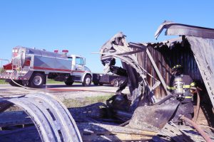 Hitting the hot spots — A Virginia volunteer firefighter hoses down hot spots inside what is left of a semi-tractor trailer destroyed in a fiery crash on Illinois Route 125 last Thursday morning.  Three people suffered non-life threatening injuries as a result of the near head-on crash. Route 125 was completely closed for nearly four hours, forcing traffic to be re-routed.  One lane traffic was still reported as late as 9 p.m. as crews worked to clear the crash scene. (Photo by Brian DeLoche