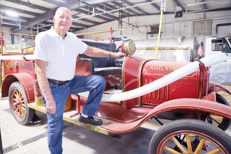A man of many hats and many years’ service — When it comes to serving the Village of Ashland, few people have served as long and in as many ways as H.A. Votsmier. He’s been a fire chief and firefighter for 31 years, water plant manager, 25 years, school board member and 911 board member. Here, Votsmier is pictured with the Ashland Fire Department’s 1923 firetruck. (Photo by Brian DeLoche.)