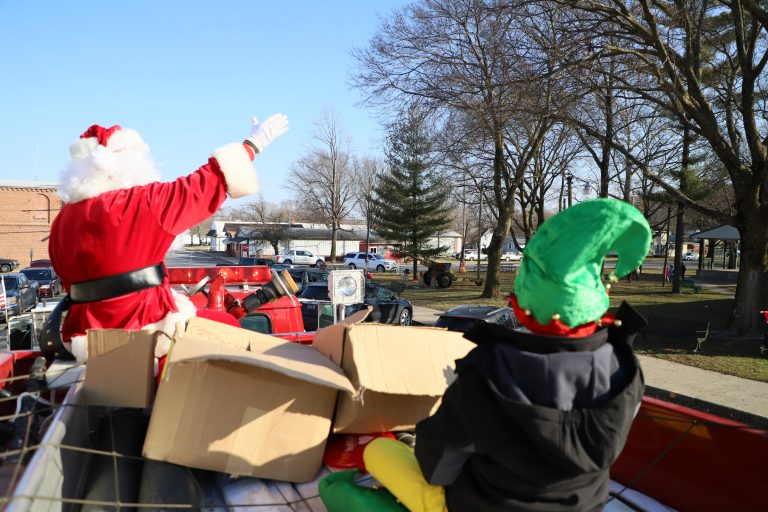 Santa, in the company of one of his most trusted elves, waves to children from the back of a firetruck as he led a caravan of emergency vehicles with lights flashing and sirens wailing through the village streets  (Photos by Brian DeLoche.)