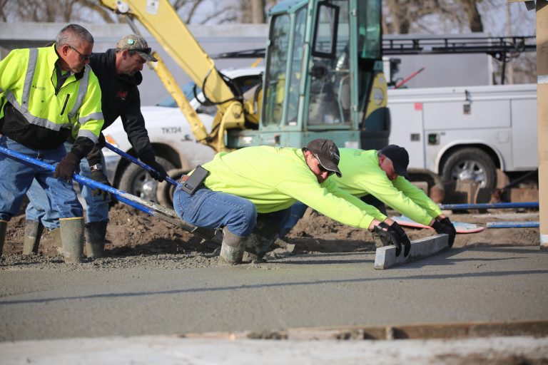 Making Progress – Work on the new campground area at the Beardstown marina continues to move forward. Construction workers for Laverdiere Construction stand ankle deep in concrete as they drag a freshly-poured section of the new pavilion floor. (Photo by Brian DeLoche.)