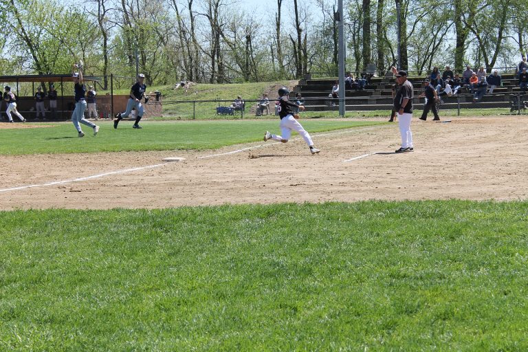 Derek Lopez rounds third on his way to home as Hall of Fame Coach Robin Lewis waves him in during the Tigers win over New Berlin at Ed Lewis field. 						 	  Photo by Jason Brockschmidt
