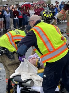 Students look on as crash reinactment victim Veronica Richards is pulled from a car Friday at Beardstown High School. The pre-prom activity is designed to give students a look at what happens at a DUI accident beginning with the initial 911 call. They watched while EMT’s removed and transported victims and the driver of the car is arrested. At the end, the coroner pulls away with the final victim.   Photo by Bill Mitchell