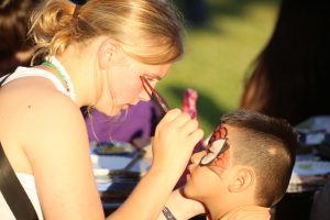 Emma Davis paints a Spiderman mask on a young man during last week’s Family Friday Carnival in the city square. The event featured bounce houses, sack races, hula hoops and sidewalk chalk art. Photo by Brian Deloche