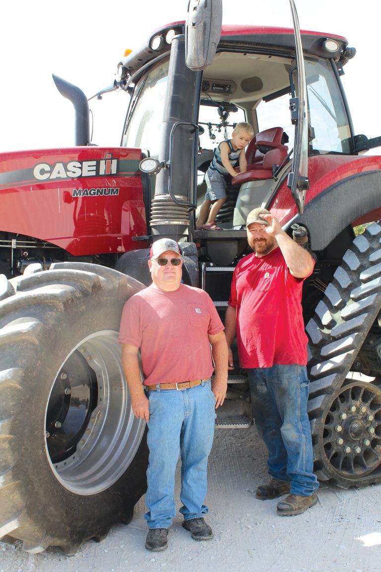 Pictured outside one of their tractors are Aaron (left) and Philip Roegge with future farmer, Harland Roegge playing inside the tractor. Photo by Michelle Carty