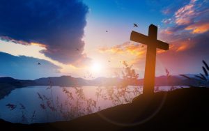 Concept conceptual black cross religion symbol silhouette in grass over sunset or sunrise sky. Focus on Faith