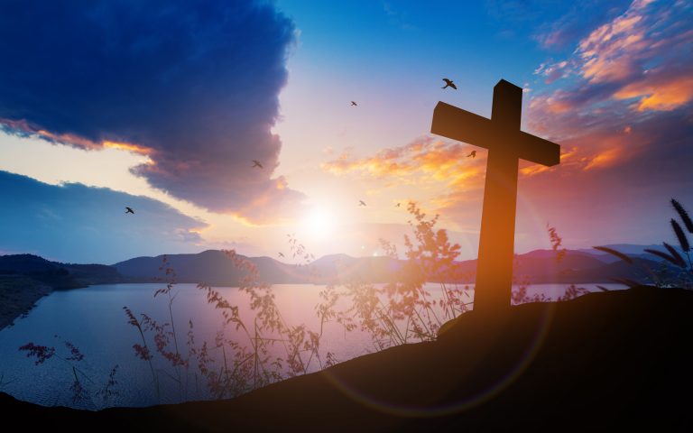 Concept conceptual black cross religion symbol silhouette in grass over sunset or sunrise sky. Focus on Faith