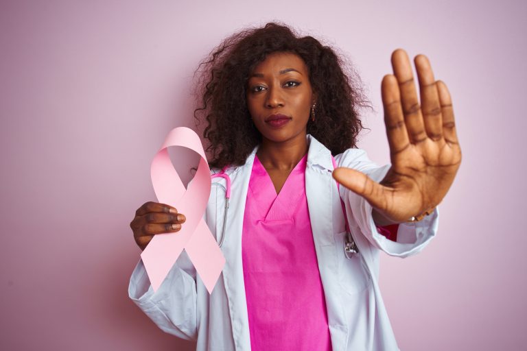 Young african american doctor woman holding cancer ribbon over isolated pink background with open hand doing stop sign with serious and confident expression, defense gesture